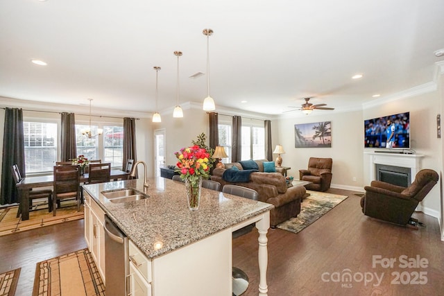 kitchen featuring light stone counters, a center island with sink, hanging light fixtures, open floor plan, and a sink