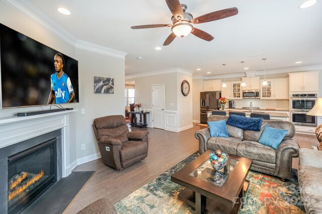 living room with dark wood-style floors, recessed lighting, a glass covered fireplace, and crown molding