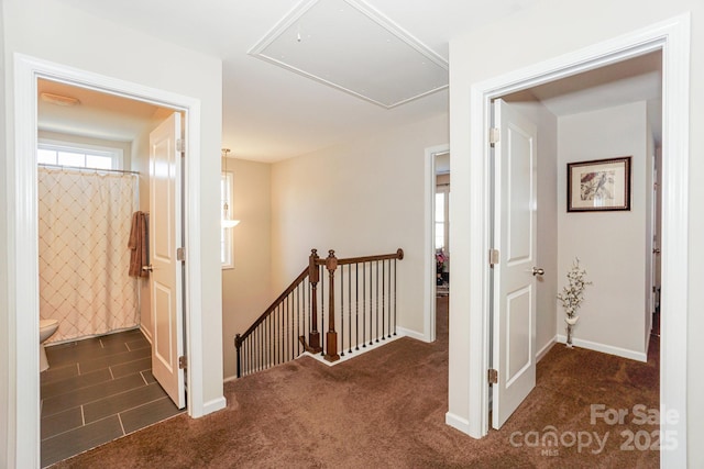 hall featuring attic access, baseboards, dark carpet, and an upstairs landing