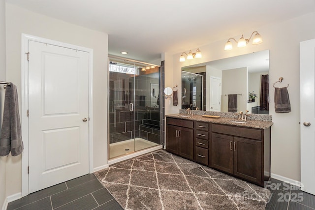 bathroom featuring a stall shower, a sink, baseboards, and double vanity