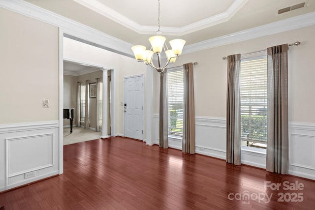 unfurnished dining area with decorative columns, visible vents, a chandelier, and wood finished floors