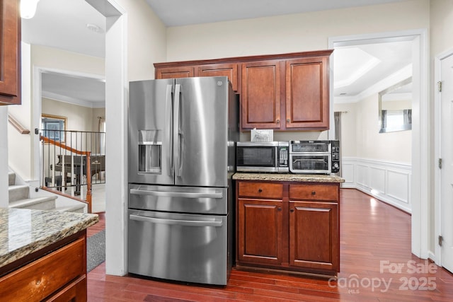 kitchen with dark wood-style floors, stainless steel appliances, a decorative wall, wainscoting, and light stone countertops