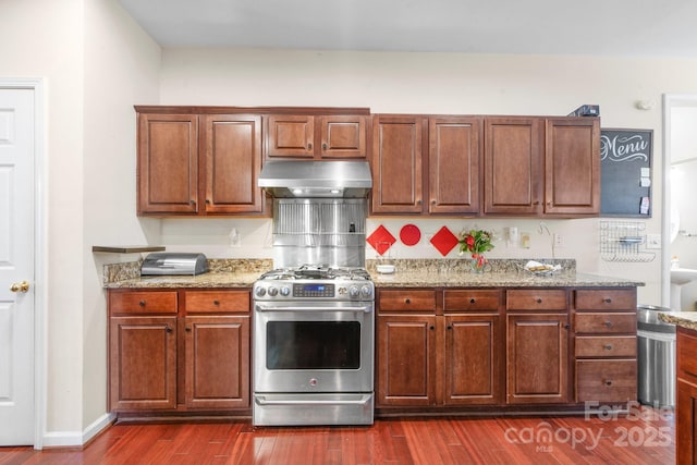 kitchen with dark wood-type flooring, exhaust hood, baseboards, light stone countertops, and stainless steel gas stove