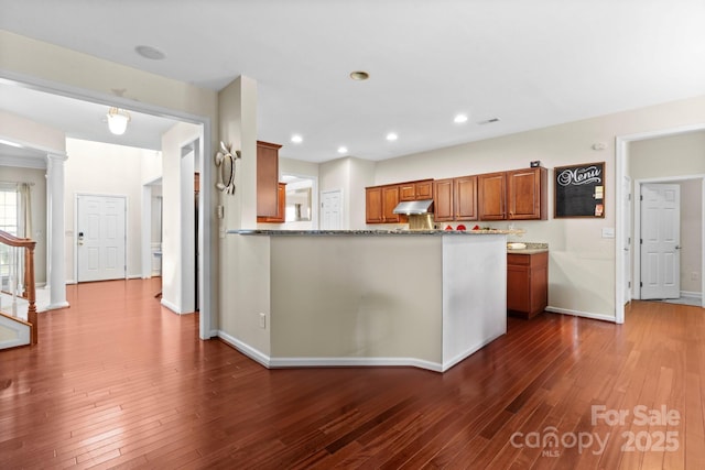 kitchen with baseboards, dark wood finished floors, brown cabinetry, under cabinet range hood, and recessed lighting