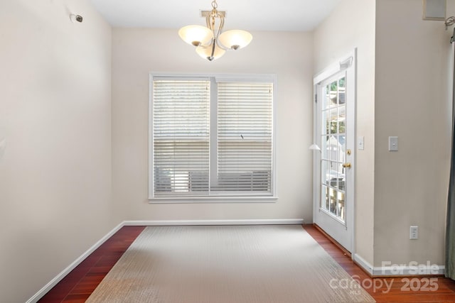 unfurnished dining area with a notable chandelier, wood finished floors, and baseboards