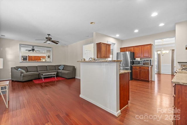 kitchen with light stone counters, recessed lighting, wood finished floors, appliances with stainless steel finishes, and brown cabinets