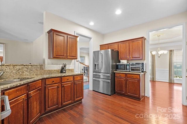 kitchen with a toaster, a sink, appliances with stainless steel finishes, light stone countertops, and dark wood finished floors