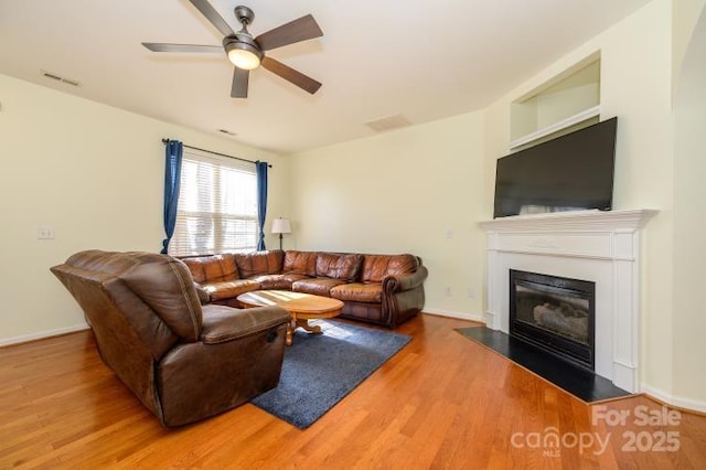 living room with wood finished floors, visible vents, baseboards, a ceiling fan, and a glass covered fireplace