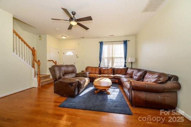 living room with visible vents, ceiling fan, wood finished floors, baseboards, and stairs