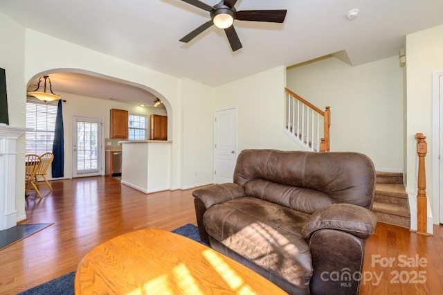 living room with baseboards, arched walkways, ceiling fan, wood finished floors, and stairs