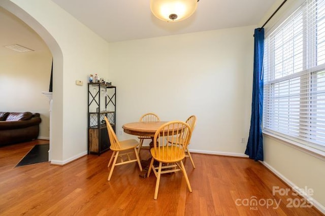 dining area with arched walkways, wood finished floors, and baseboards