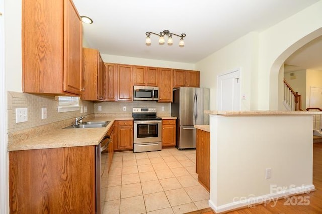 kitchen featuring tasteful backsplash, appliances with stainless steel finishes, brown cabinets, light countertops, and a sink