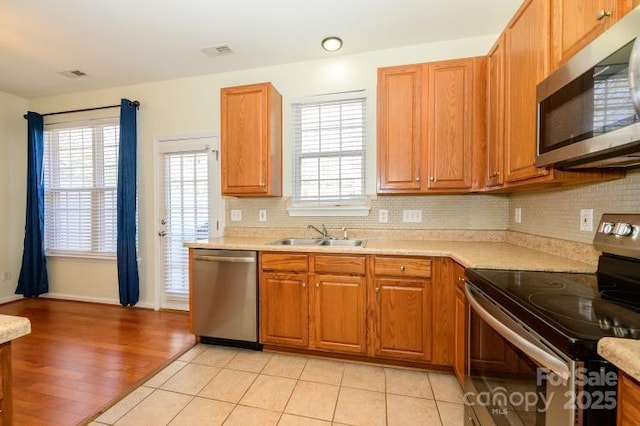 kitchen with light countertops, appliances with stainless steel finishes, brown cabinetry, and a sink