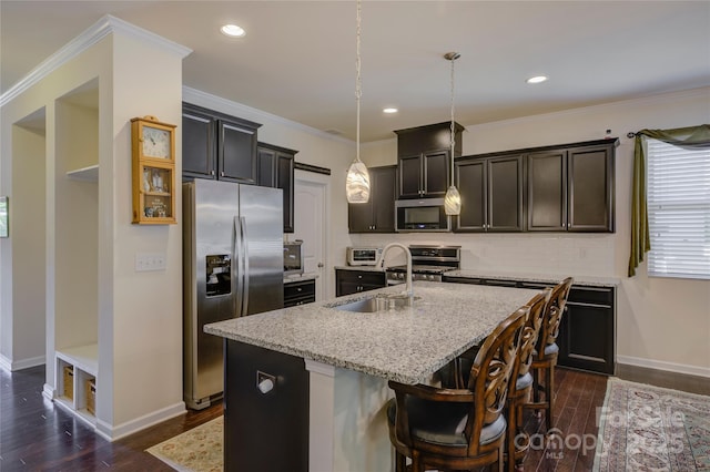 kitchen featuring a kitchen island with sink, light stone counters, stainless steel appliances, and decorative light fixtures