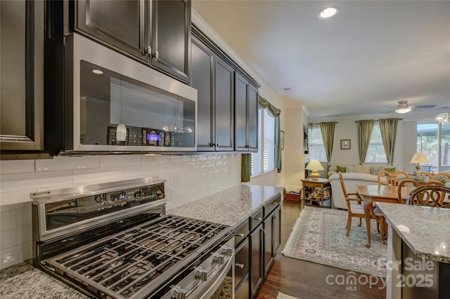 kitchen with light stone counters, dark wood-style floors, tasteful backsplash, appliances with stainless steel finishes, and dark brown cabinets