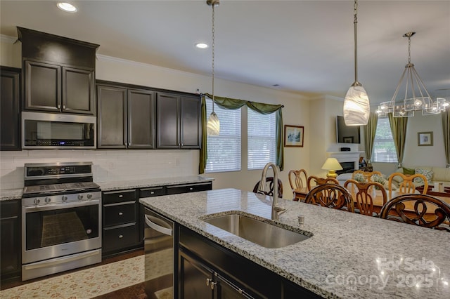 kitchen with light stone counters, stainless steel appliances, a sink, hanging light fixtures, and backsplash