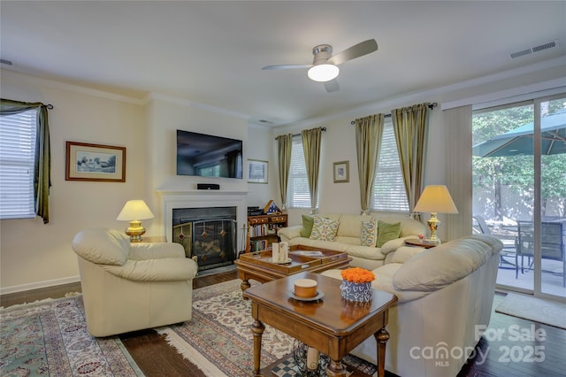 living room with wood finished floors, a glass covered fireplace, visible vents, and crown molding