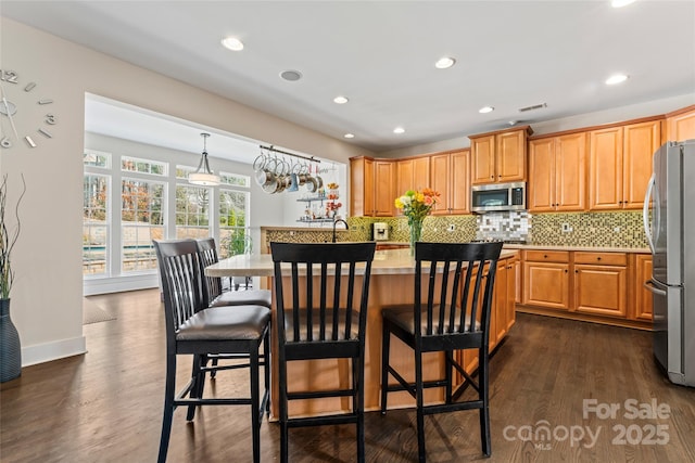 kitchen featuring dark wood-style floors, stainless steel appliances, light countertops, decorative backsplash, and a kitchen island