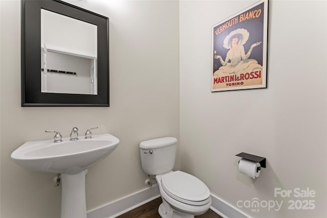 half bathroom with toilet, baseboards, and a sink