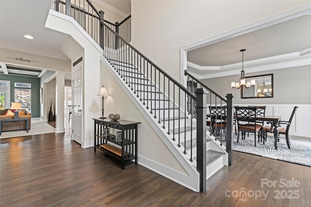 stairway with ornamental molding, wood finished floors, decorative columns, and an inviting chandelier