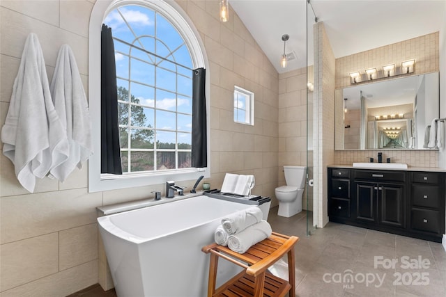 bathroom with lofted ceiling, tile patterned flooring, toilet, tile walls, and a soaking tub