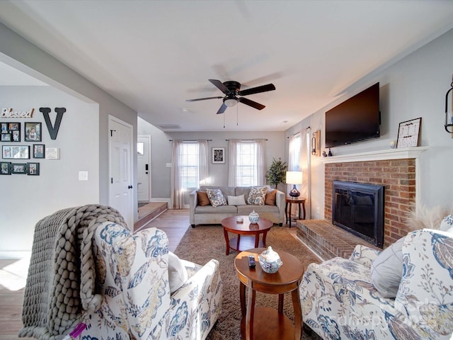 living room featuring a brick fireplace, ceiling fan, and wood finished floors