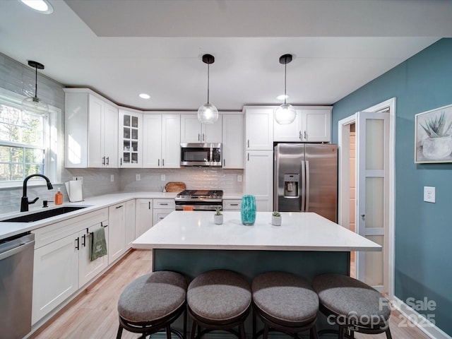 kitchen with a sink, white cabinets, a kitchen breakfast bar, appliances with stainless steel finishes, and decorative backsplash