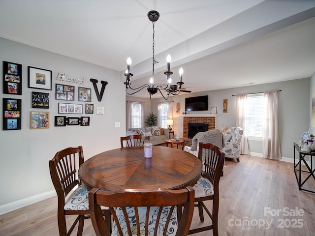 dining room with light wood-type flooring, a brick fireplace, baseboards, and an inviting chandelier