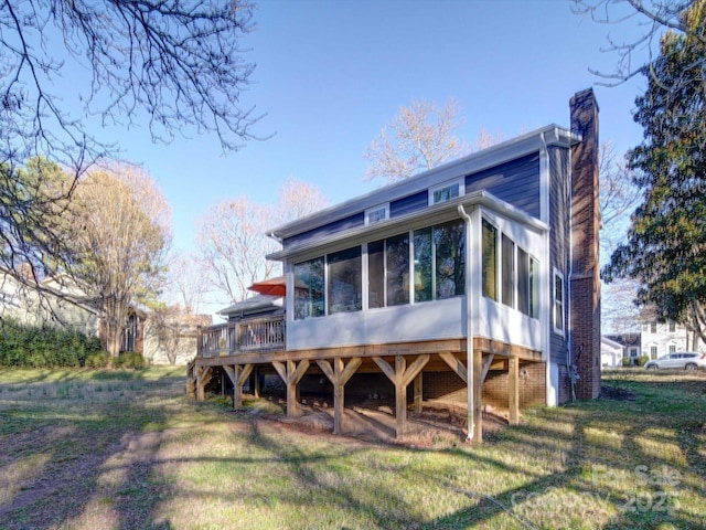 rear view of house featuring a sunroom, a lawn, and a chimney