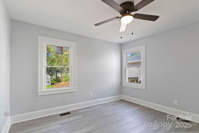 unfurnished room with wood finished floors, visible vents, and a wealth of natural light