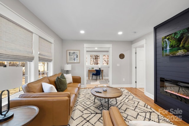 living area featuring light wood finished floors, recessed lighting, a large fireplace, and baseboards