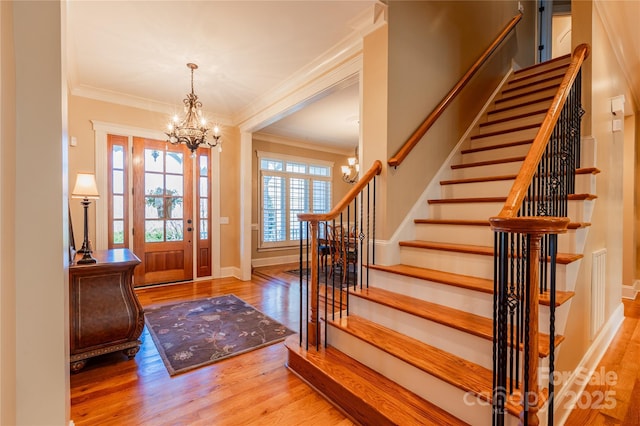 foyer entrance with an inviting chandelier, ornamental molding, wood finished floors, baseboards, and stairs