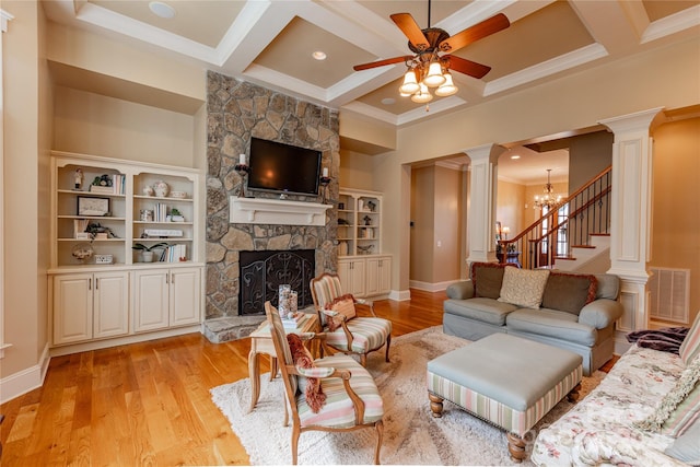 living area featuring decorative columns, coffered ceiling, light wood-type flooring, a fireplace, and ceiling fan with notable chandelier