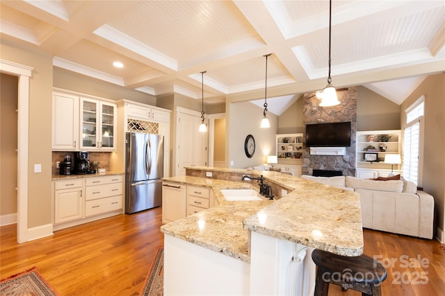 kitchen featuring light wood-style floors, freestanding refrigerator, glass insert cabinets, a sink, and a kitchen bar