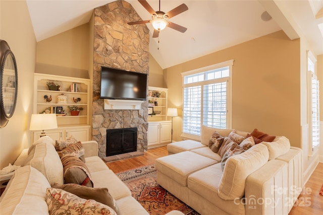 living room with high vaulted ceiling, a stone fireplace, wood finished floors, and a ceiling fan