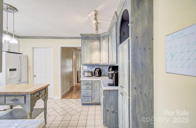 kitchen featuring tasteful backsplash, light countertops, hanging light fixtures, and a textured ceiling