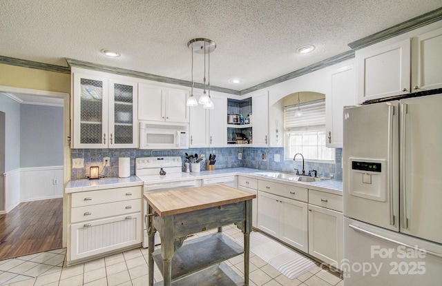 kitchen featuring white appliances, a sink, white cabinets, glass insert cabinets, and pendant lighting