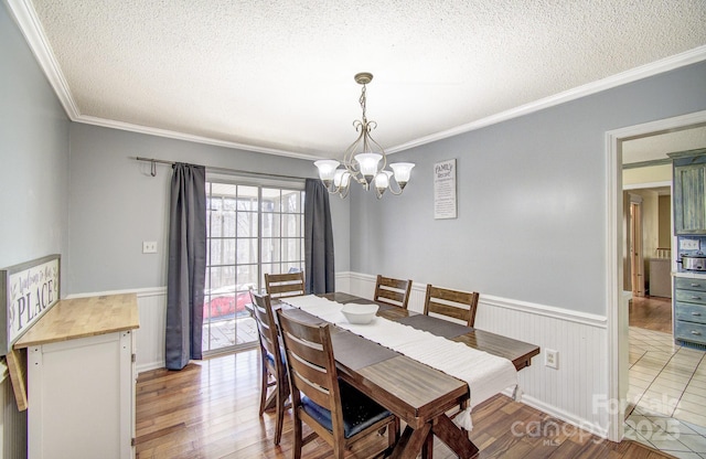 dining space featuring a textured ceiling, light wood finished floors, wainscoting, and an inviting chandelier