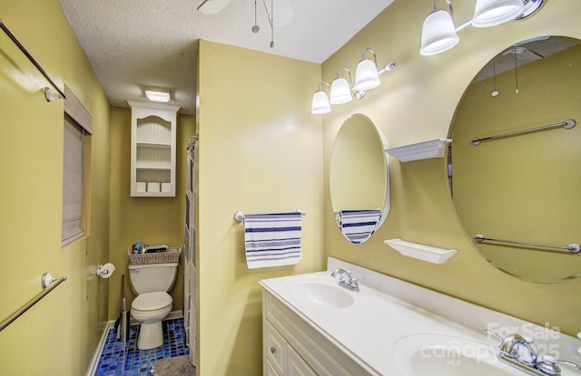 full bath featuring toilet, double vanity, a textured ceiling, and a sink