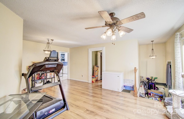 workout area with light wood-type flooring, ceiling fan, a textured ceiling, and baseboards