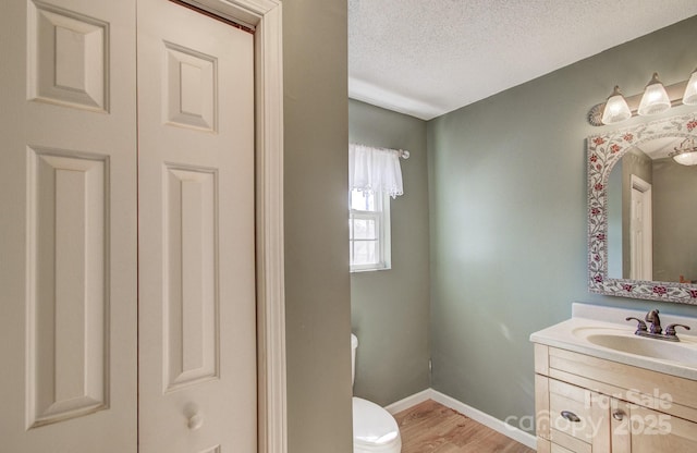 bathroom featuring a textured ceiling, toilet, wood finished floors, vanity, and a closet