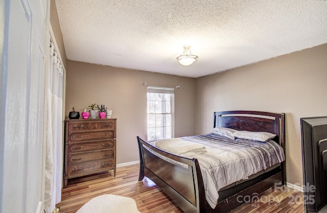 bedroom featuring light wood-style flooring, baseboards, and a textured ceiling