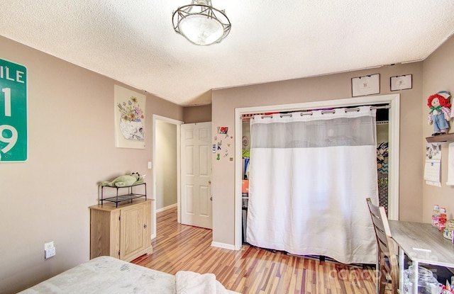 bedroom featuring light wood-type flooring, a closet, a textured ceiling, and baseboards