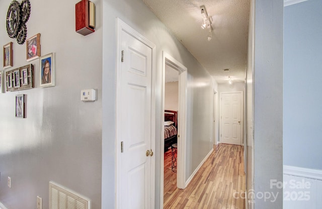 hall featuring track lighting, visible vents, a textured ceiling, and light wood finished floors