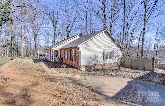 view of side of home featuring a porch, crawl space, fence, and brick siding