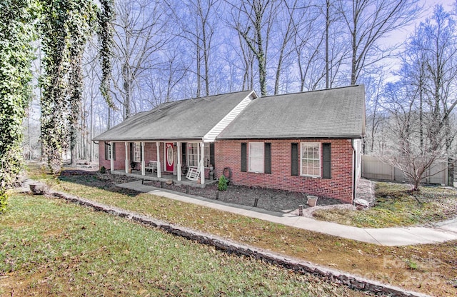 view of front of house featuring a shingled roof, a front yard, a porch, and brick siding