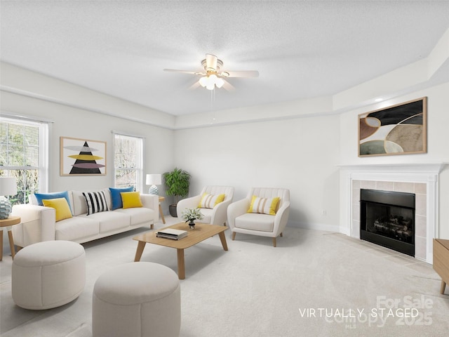 carpeted living room featuring a textured ceiling, ceiling fan, a tiled fireplace, and baseboards