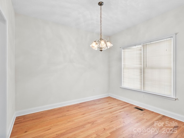 unfurnished room featuring baseboards, visible vents, light wood finished floors, and an inviting chandelier