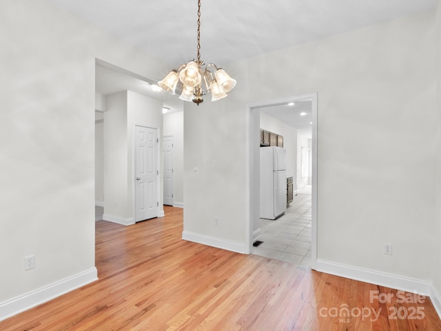 unfurnished dining area featuring baseboards, light wood finished floors, and an inviting chandelier