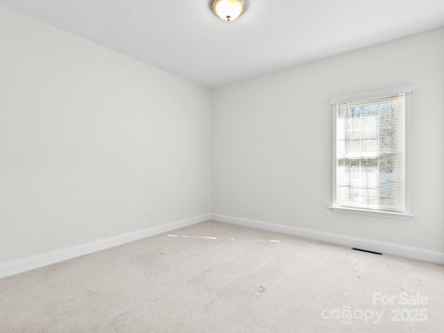 empty room with light carpet, a textured ceiling, visible vents, and baseboards